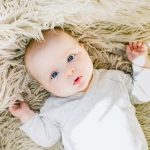 Baby with bright blue eyes laying on carpet